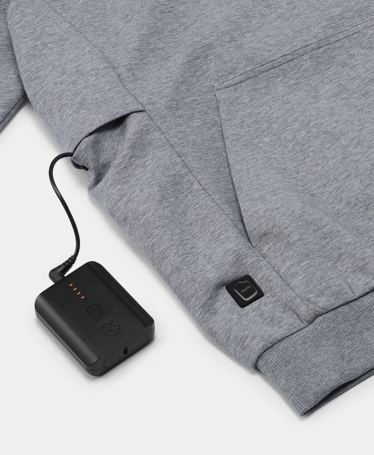 A flecking gray Toasty Unisex 5-Zone Heated Pullover Hoodie, displaying a close-up of the illuminated power button near the hem, connected to a rechargeable battery stored in the right-side exterior pocket.