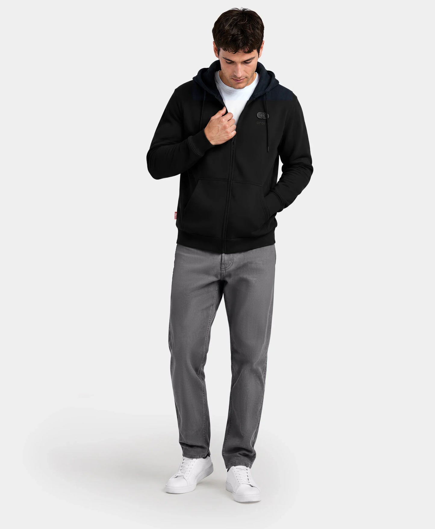 A man standing with hands in pockets wearing the black SureWarm? Unisex 6-Zone Fleece Heated Hoodie with gray pants