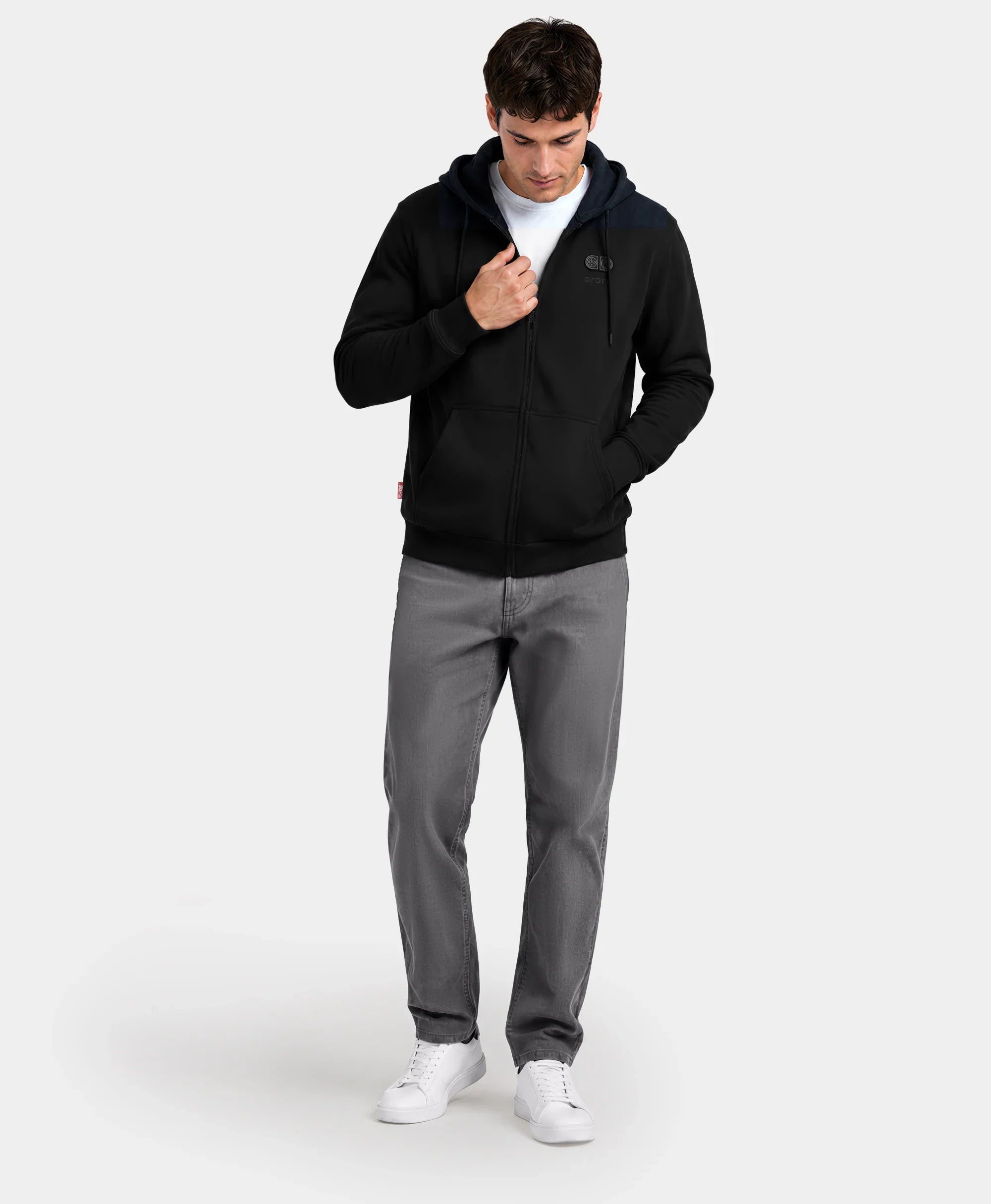 A man standing with hands in pockets wearing the black SureWarm? Unisex 6-Zone Fleece Heated Hoodie with gray pants