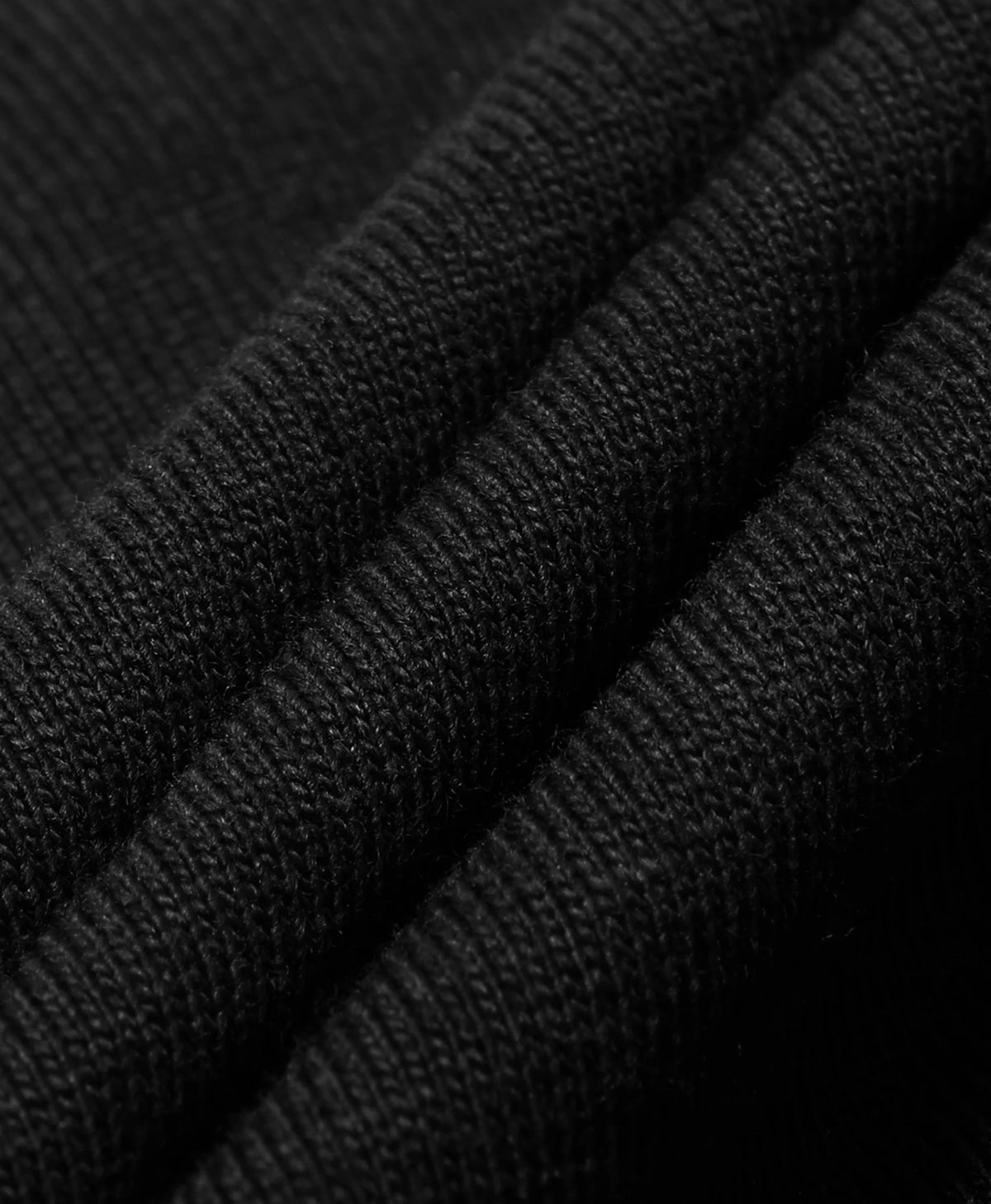 A close-up of black ribbed knit fabric with soft diagonal folds showing the texture and weave.